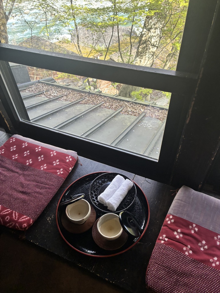 Welcome tea set on a black tray with white hand towels, beside a window view of the river at Yarimikan ryokan in Okuhida
