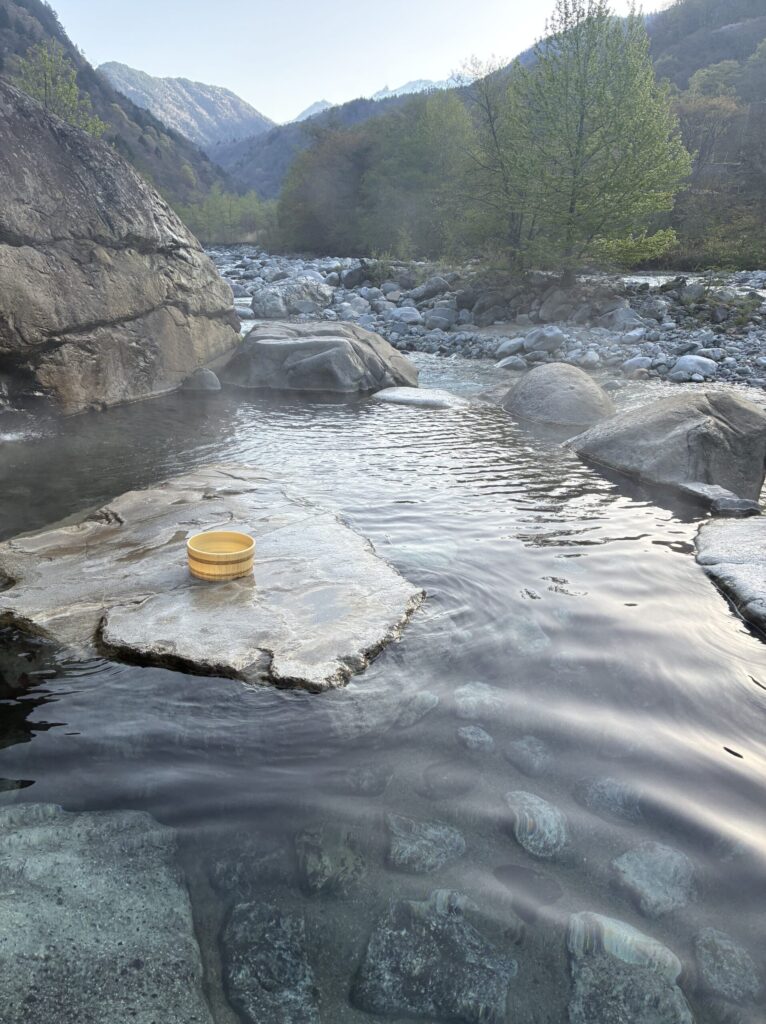 Outdoor stone-walled onsen bath surrounded by mountain forest at Yarimikan ryokan in Okuhida